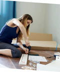 Person assembling furniture with tools and instructions on the floor, surrounded by hardware and packaging.