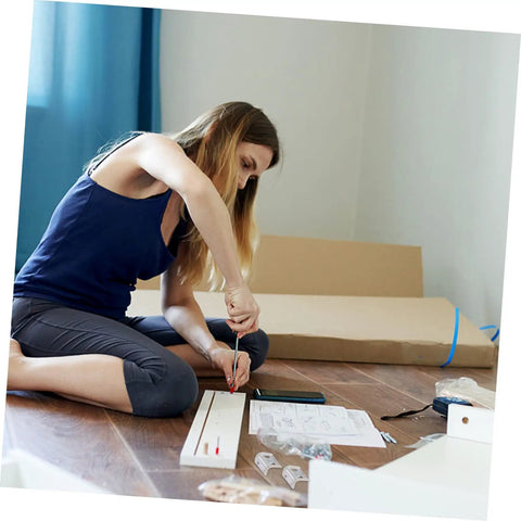 Person assembling furniture with tools and instructions on the floor, surrounded by hardware and packaging.