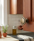 25 Pack Brushed Antique Brass Round Cabinet Knobs, One And A Quarter Inch Diameter, One Inch Projection, mounted on wooden cabinet door