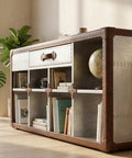 Sharp Aviator Bookcase Featuring Hand Beaten Aluminum Build And Single Storage Drawer Heavy Duty Industrial Home Office Shelves 60 Inches Tall in a sunlit room with plants.