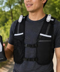 Person wearing Hands Free Hydration Running Vest With 500ml Soft Flask BPA Free PVC Free Reflective Gear Adjustable Unisex Fit 4 LED Lights 6 Pockets For Running Accessories Perfect Gear For Runners On The Go holding black soft flask outdoors.