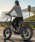 Woman riding Beast Electric Bike For Adults With 1800W Peak Motor, 86 Mile Range, 52V 18.2Ah Removable Battery along coastal road.