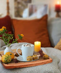 Acacia wood serving tray on a sofa with a blue mug, four muffins, two decorative pumpkins, and a vase of yellow flowers