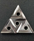 Four triangular carbide inserts with central holes, metal gray, for lathe turning and grooving.