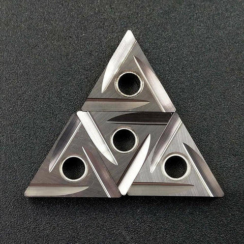 Four triangular carbide inserts with central holes, metal gray, for lathe turning and grooving.