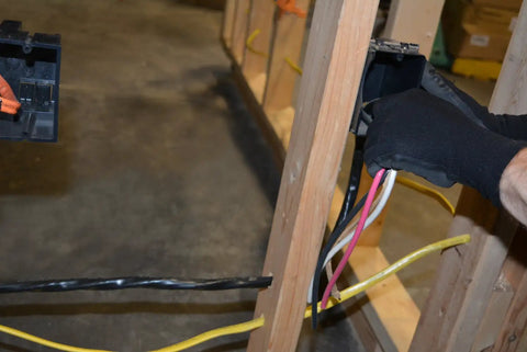 Electrician installs 25 Ft 6-3 NM-B Cable NMWG Ground For Residential In-Wall Wiring in wooden frame, using gloved hand.