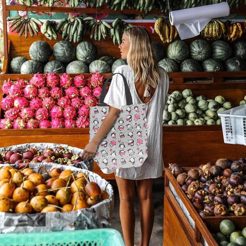 Woman shopping at market with collapsible trolley bag with wheels for groceries, wearing a light dress, tropical fruits in background.