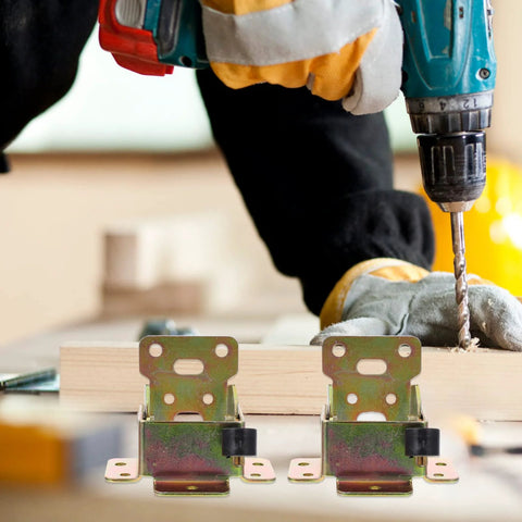 Two folding iron hinge brackets for furniture legs on wood surface; zinc-plated metal with mounting holes.