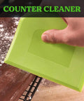 Close-up of hand using green piece from 3-Piece Flexible Dough Scraper Bench Set, 4.7x3.7 Inch Bowl Scraper With Sharp Edge And Angles, Non-Slip Bakeware Tool For Kneading, Scraping, Decorating, Sculpting And Modeling, Green White Green, on wooden surface.
