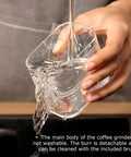 Hand pouring water into a clear cup, showcasing usability for cleaning the Road Trip Ready Portable Electric Coffee Grinder With Adjustable Stainless Steel Burrs, USB Rechargeable One Touch Auto Stop, No Sweat Brewing For Espresso To French Press, Collapsible Hopper In Black.