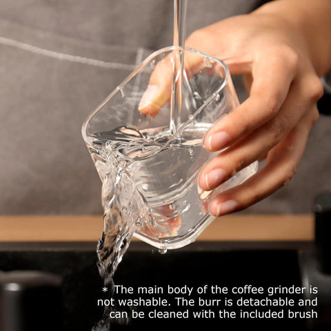 Hand pouring water into a clear cup, showcasing usability for cleaning the Road Trip Ready Portable Electric Coffee Grinder With Adjustable Stainless Steel Burrs, USB Rechargeable One Touch Auto Stop, No Sweat Brewing For Espresso To French Press, Collapsible Hopper In Black.