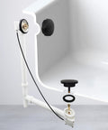 Heavy Duty Matte Black Bath Drain Plug With A Slick 35 Inch Cable Drive Pop Up Mechanism and Solid Brass Handle installed in a tub.