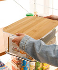 Person placing Clear PET Plastic Storage Bins With Removable Bamboo Lids And Grab Handles on a shelf, visible contents inside.