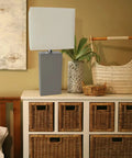 Leather Wrapped Modern Table Lamp With White Fabric Shade In Gray on dresser with woven baskets and decor