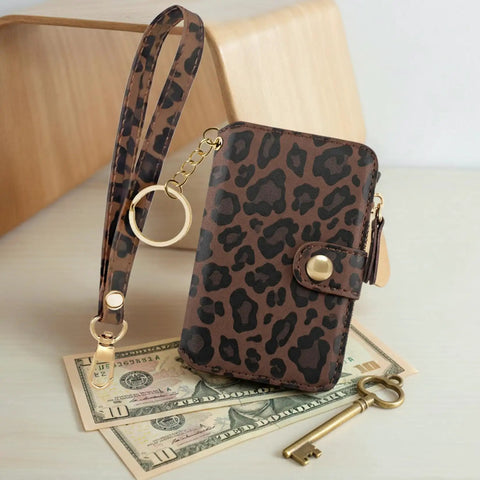 Streamlined Rfid Blocking Keychain Wallet With Genuine Leather Wrist Strap resting on bills, featuring a leopard print design.