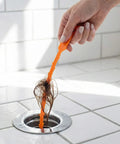 Hand using 4 Pack 25 Inch Drain Snake Kit For Clogged Drains And Drain Clog Remover Unclog Kitchen Sink Bathroom Tub Toilet With Flexible 0.45 Inch Barbed Wand to remove hair from shower drain.