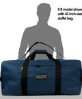 Beast Heavy Duty Cargo Duffel 170L Large Sport Gear Bag next to 6 ft model for size comparison, water resistant, square design.