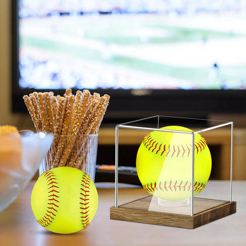 Clear Acrylic Softball Display Case With Wood Base For One Ball on table, next to glass with pretzels, with TV in background.