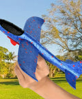 Blue foam glider plane held in hand in park, 7.68 inch, lightweight, suitable for outdoor play. Foam Gliders For Backyard Fun And Outdoor Play Lightweight 7.68 Inch Foam Launchers For Kids Totally Easy Toss Soaring Summer Recreation Beach And Park Entertainment Safe Compact Planes That Boost Hand Eye Coordination.