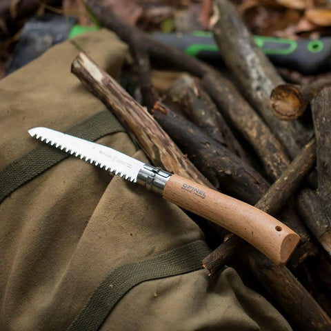 Badass Lightweight Folding Saw For Weekend Campouts And Garden Grind Cuts Branches Fast With Razor Sharp Carbon Steel Blade Secure Virobloc Lock And Natural Beechwood Handle on fabric with twigs in background.