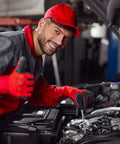 Mechanic in red uniform working under car hood in a garage, giving thumbs up.