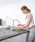 Clean Lines Single Handle Pull Out Kitchen Faucet With Laminar Spray Led Knobs For Chilled Sparkling Water Butter Smooth Pour 180 Swivel Spout in modern kitchen, woman rinsing vegetables.