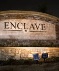 Outdoor Solar Flood Light in Black Cast Aluminum with Warm White 2700K LEDs uplighting a stone wall with a solar panel