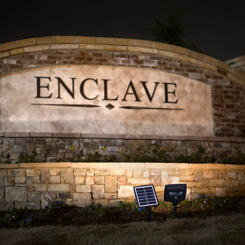 Outdoor Solar Flood Light in Black Cast Aluminum with Warm White 2700K LEDs uplighting a stone wall with a solar panel
