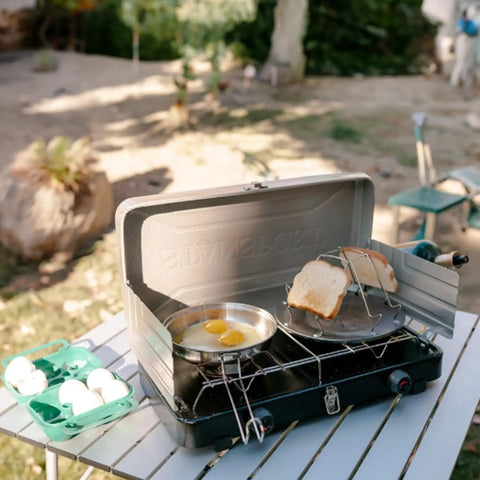 Portable stovetop camping toaster with four slices on a gas stove, stainless steel, ideal for outdoor cooking and picnics.