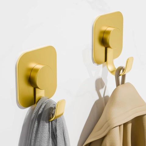 Heavy Duty Adhesive Wall Hooks In A Dope Four Pack, Stainless Steel Stick On Hangers With Badass Grip For Bathrooms And Kitchens, Waterproof And Super Fast To Put Up On Any Wall Or Door Without Drilling, Classic Gold Finish hanging towels on a white wall.