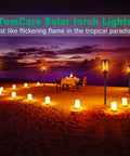43 Inch Solar Flameless LED Torches With Flickering Flame Effect illuminating a beach setting with chairs and table at sunset