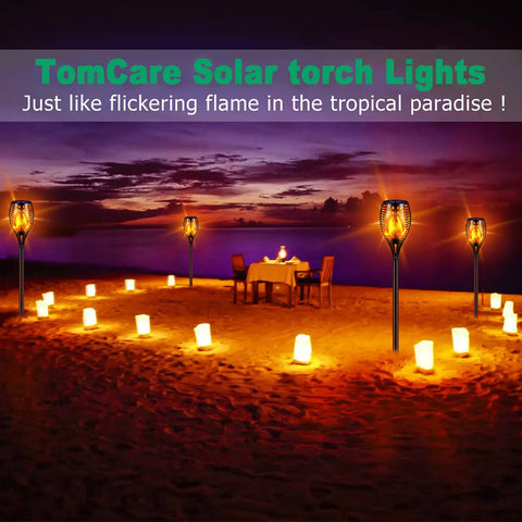 43 Inch Solar Flameless LED Torches With Flickering Flame Effect illuminating a beach setting with chairs and table at sunset