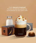 Glass mug of Nespresso coffee with milk froth and caramel pieces, alongside Vertuo capsules and a milk bottle.