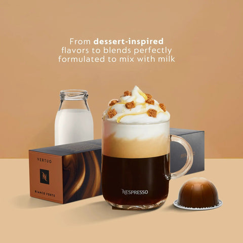 Glass mug of Nespresso coffee with milk froth and caramel pieces, alongside Vertuo capsules and a milk bottle.