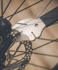 Close-up of a Two In One Disc Rotor Truing Fork And Caliper Piston Press Spreading Tool Wrench And Ratchet in use on bike brakes.