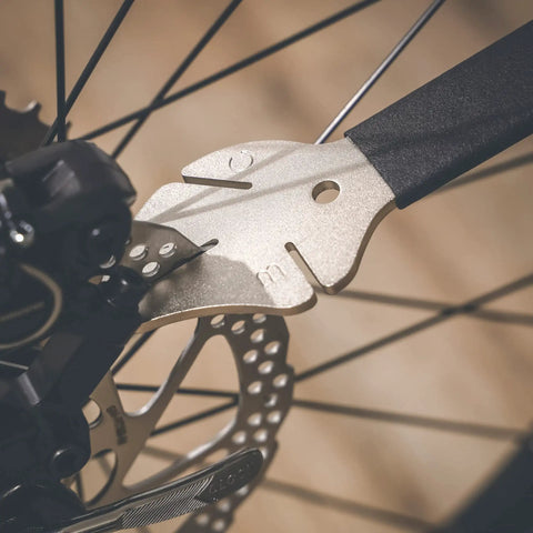 Close-up of a Two In One Disc Rotor Truing Fork And Caliper Piston Press Spreading Tool Wrench And Ratchet in use on bike brakes.