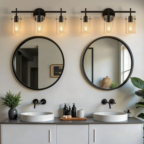 Modern bathroom scene with two three light matte black vanity lights with clear glass shades over round mirrors and vanities.