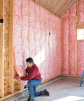 Man installing Premium Pink Fiberglass Insulation Batts For Interior Walls And Attic Cavities in a framed space.