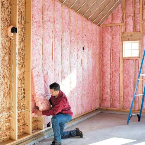 Man installing Premium Pink Fiberglass Insulation Batts For Interior Walls And Attic Cavities in a framed space.
