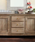 Wooden sideboard with drawers and cabinets featuring brass knobs and handles, decorated with glassware and a fruit display.