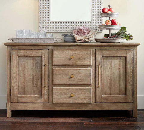 Wooden sideboard with drawers and cabinets featuring brass knobs and handles, decorated with glassware and a fruit display.