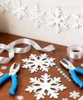 Adjustable Handheld Circle Hole Punch for crafts with blue soft grip on table, surrounded by snowflake cutouts and ribbons.