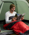 Person sitting in tent using Cozy Cold Weather Sleeping Bag For Adults Perfect For Backpacking And Camping Lightweight And Packable Gear For Hiking Waterproof 190T Polyester Shell Durable Red.