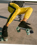 Person skating in yellow pants wearing quad roller skates with Adjustable Elastic Brake Block For Quad Roller Skates And Ice Skates Rubber Brake Stopper Kit With Easy Install Tool For Women Men Boys And Girls Universal Skating Brake System