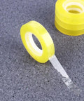 Dope 12 Pack 11mm X 30m BOPP Packing Tape, transparent roll on grey surface, easy to cut and refill, strong adhesive visible