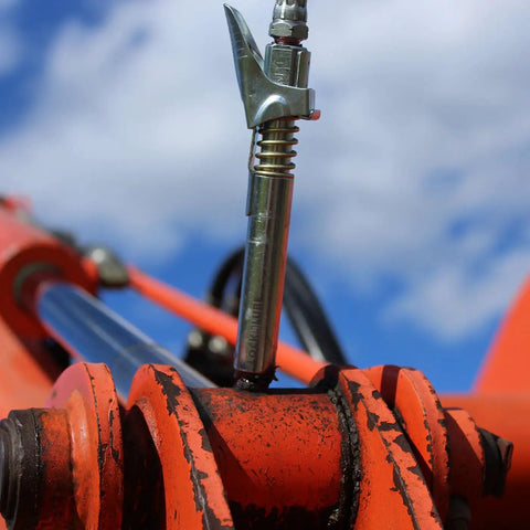 Grease Gun Coupler XL Universal Fit With 3.5 Inch Extra Reach for recessed fittings, attached to orange machinery, locking jaws visible