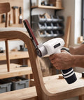 Badass Cordless Belt Sander With Brushless Motor and Rotating Head used on wood chair leg for sanding, showing dust in workshop.