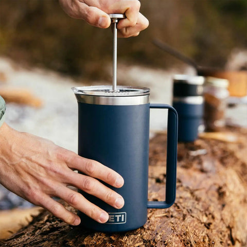 Person using Rambler 34 Oz French Press Coffee Maker With Grounds Control Filter Navy Double Wall Vacuum Insulation Keeps Your Brew Hot On The Go Easy Pour Durable Build For Everyday Boss Coffee Experience outdoors on wooden surface