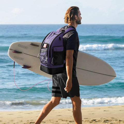 Man carrying a surfboard on the beach wearing 35L Waterproof Swim Backpack With Separate Shoes Compartment, ultra spacious purple sports rucksack