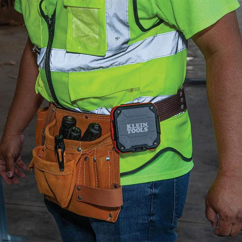 Rugged Bluetooth Speaker With Magnetic Strip And Hook attached to worker's belt at construction site, hands-free use.